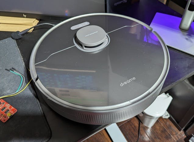 Photo of the Z10 Pro vacuum robot sitting on a desk. a red circuit board with wires sticking out of it is partially visible on the desk to the left of the robot.