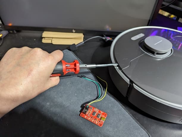 Photo of the Z10 Pro vacuum on a desk. I'm holding a flathead screwdriver and using it to pry off one of the robot's top panels.