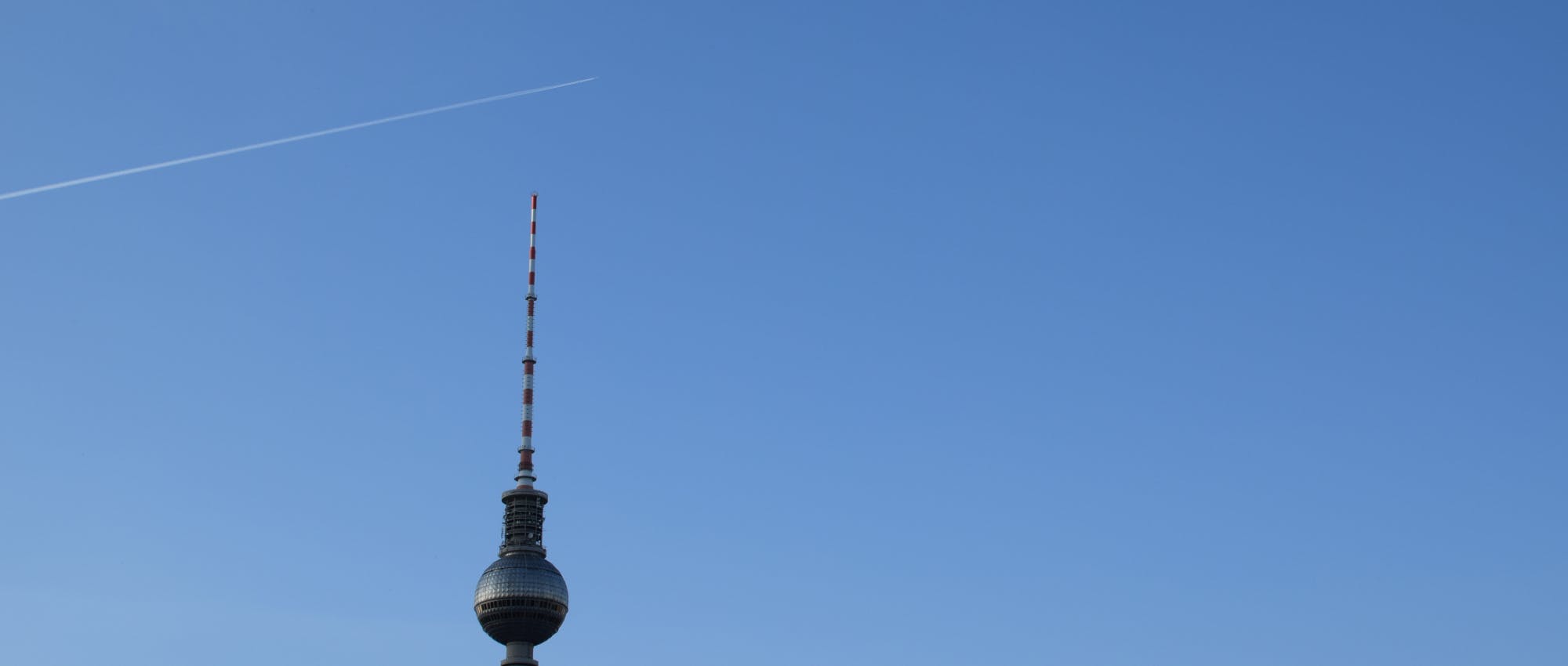 A photo of the Berlin TV tower with contrails in the sky. Shot on a Nikon D3300 with a 35mm f/1.8 lens by Xe Iaso.